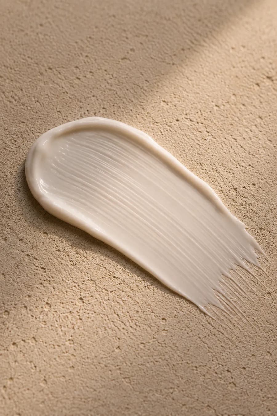 Macro of a silky Niacinamide cream swatch smoothed across a sand-coloured surface.