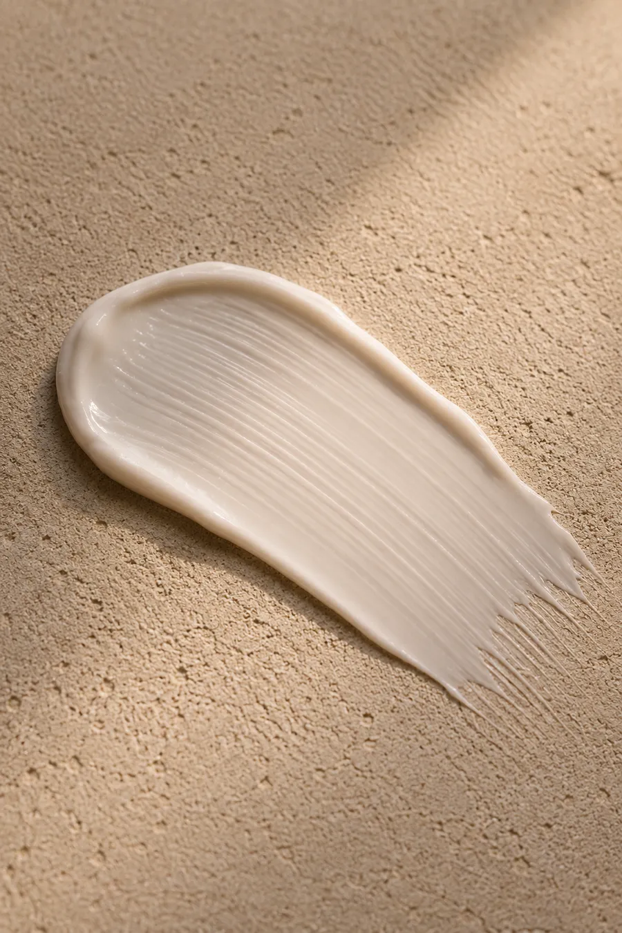 Macro of a silky Niacinamide cream swatch smoothed across a sand-coloured surface.